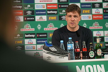 Clemens Fritz vor einer Sponsorenwand am Mikrofon.