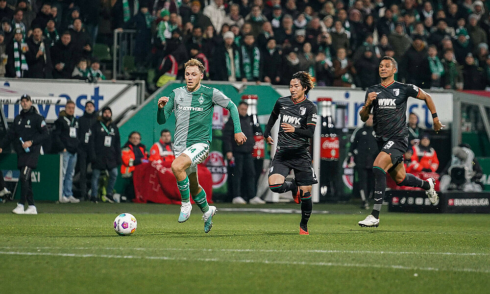 Senne Lynen wird mit Ball am Fuß von zwei Augsburger verfolgt. 