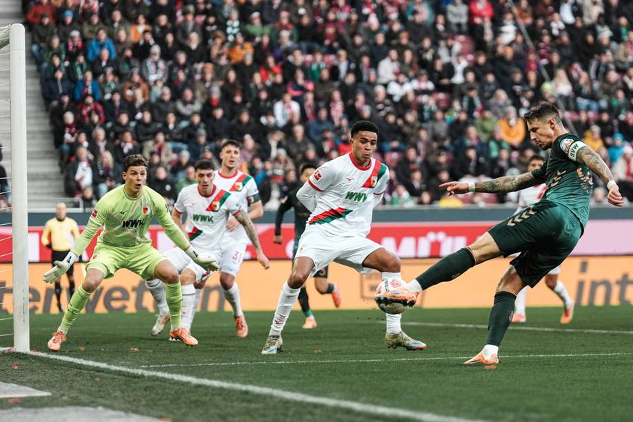 Marco Friedl gibt einen Torschuss ab, die Augsburger haben den Blick auf ihn gerichtet.