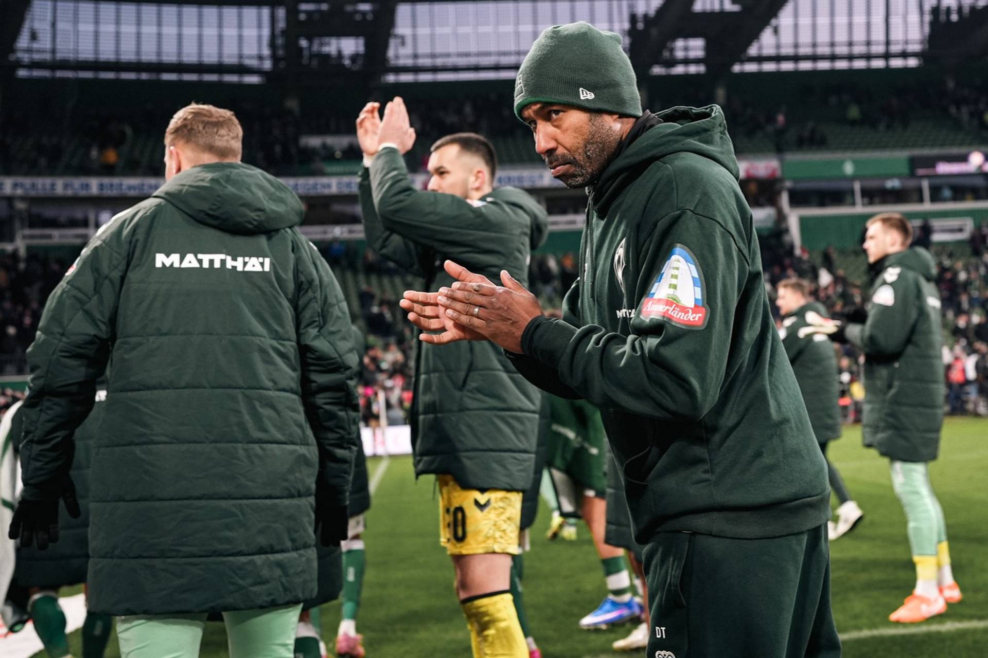 Daniel Thioune klatscht in Richtung der Fans, er trägt einen Werder-Pullover und eine Mütze.