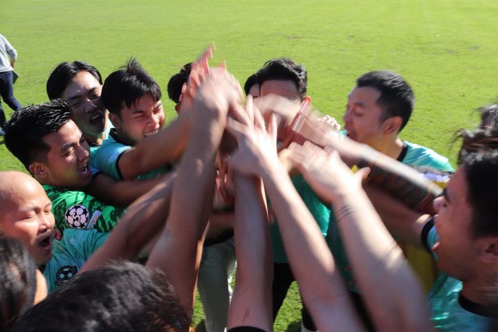 Eine Gruppe von Fußballspielern in grünen Trikots feiert ausgelassen und reckt gemeinsam die Hände in die Höhe, mitten auf einem Rasenfeld.
