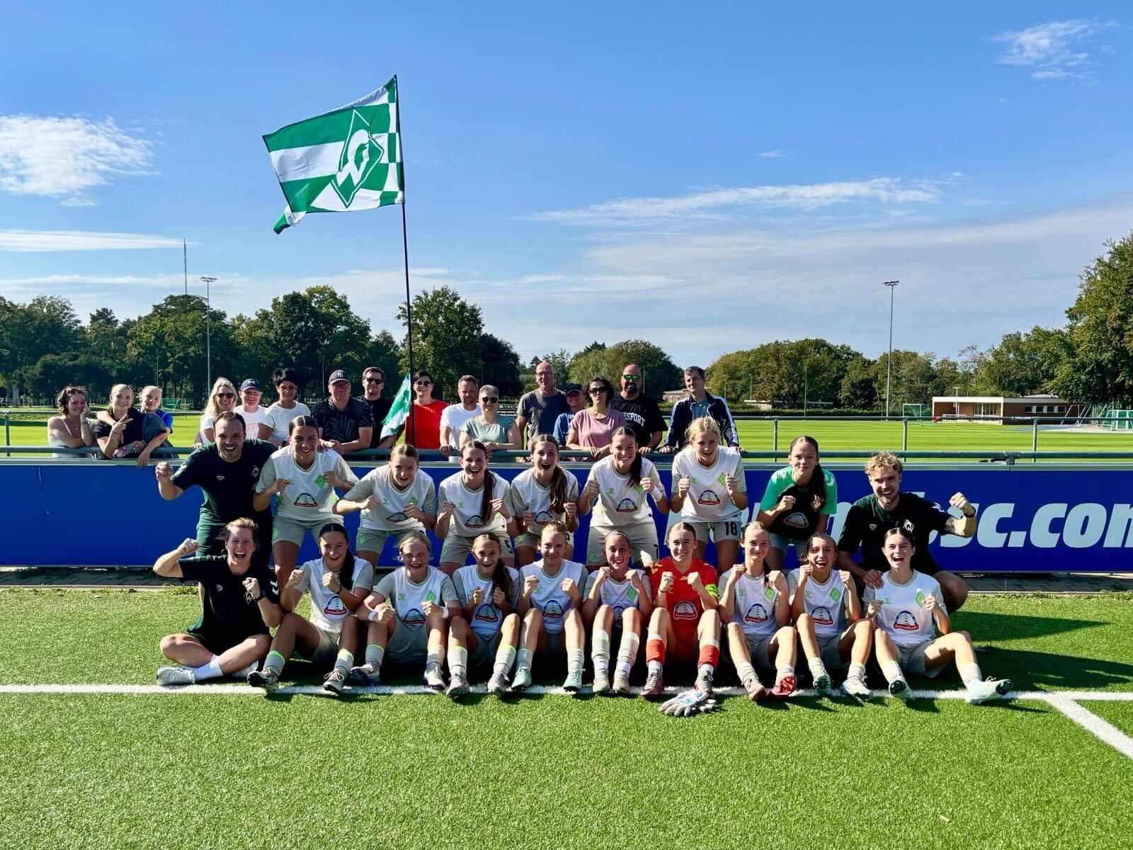 Die U17-Juniorinnen jubeln gemeinsam mit einer gehissten Werder-Flagge auf dem Platz von Hertha BSC.
