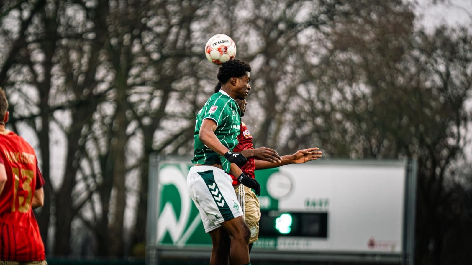 Ein Werder-Spieler ist im Vordergrund zu sehen, im Kopfballduell mit einem Gegner im roten Trikot der fast vollständig verdeckt ist.