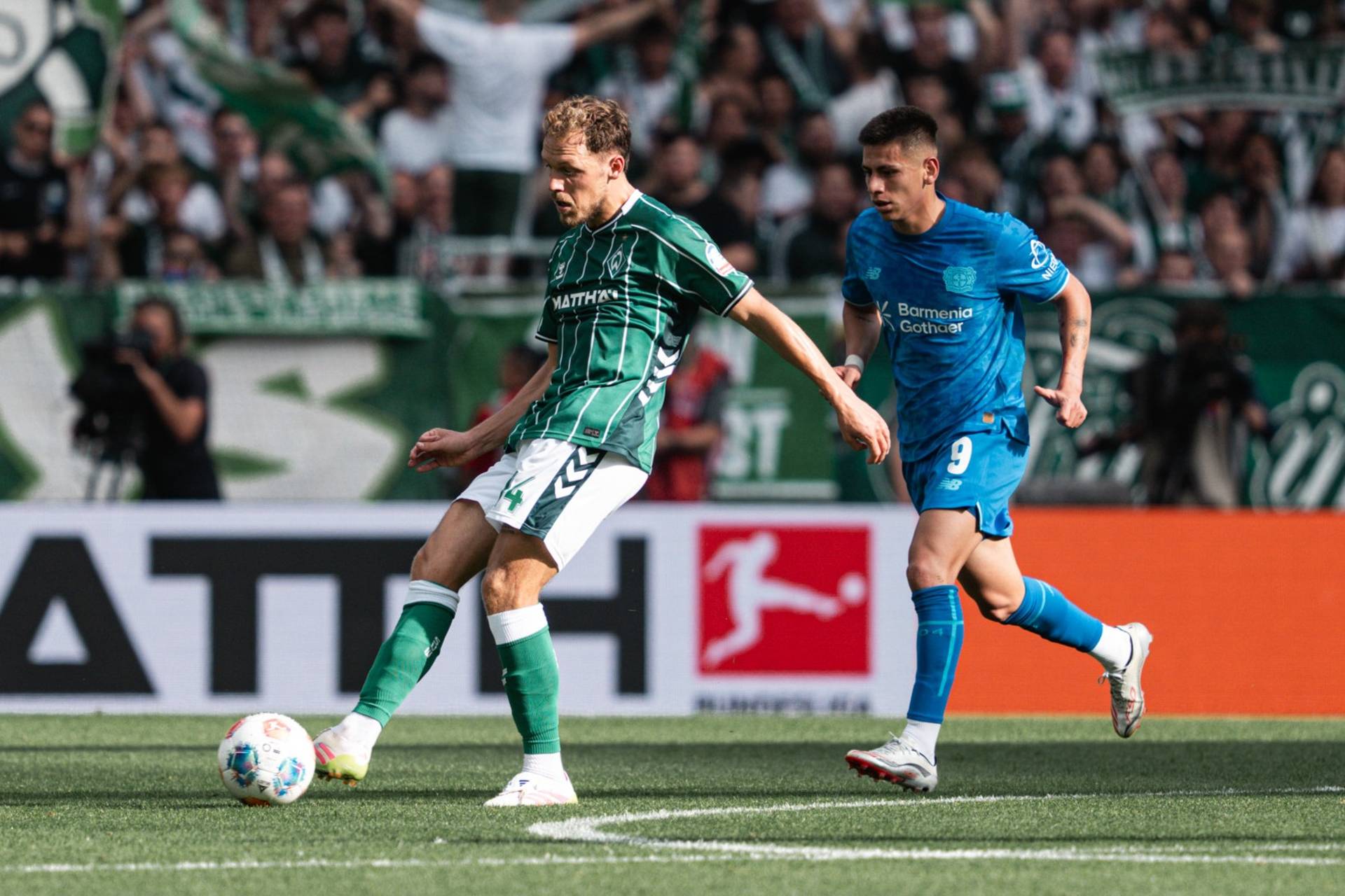 Senne Lynen im grünen Trikot passt den Ball, hinter ihm läuft ein blau gekleideter Leverkusen-Spieler.