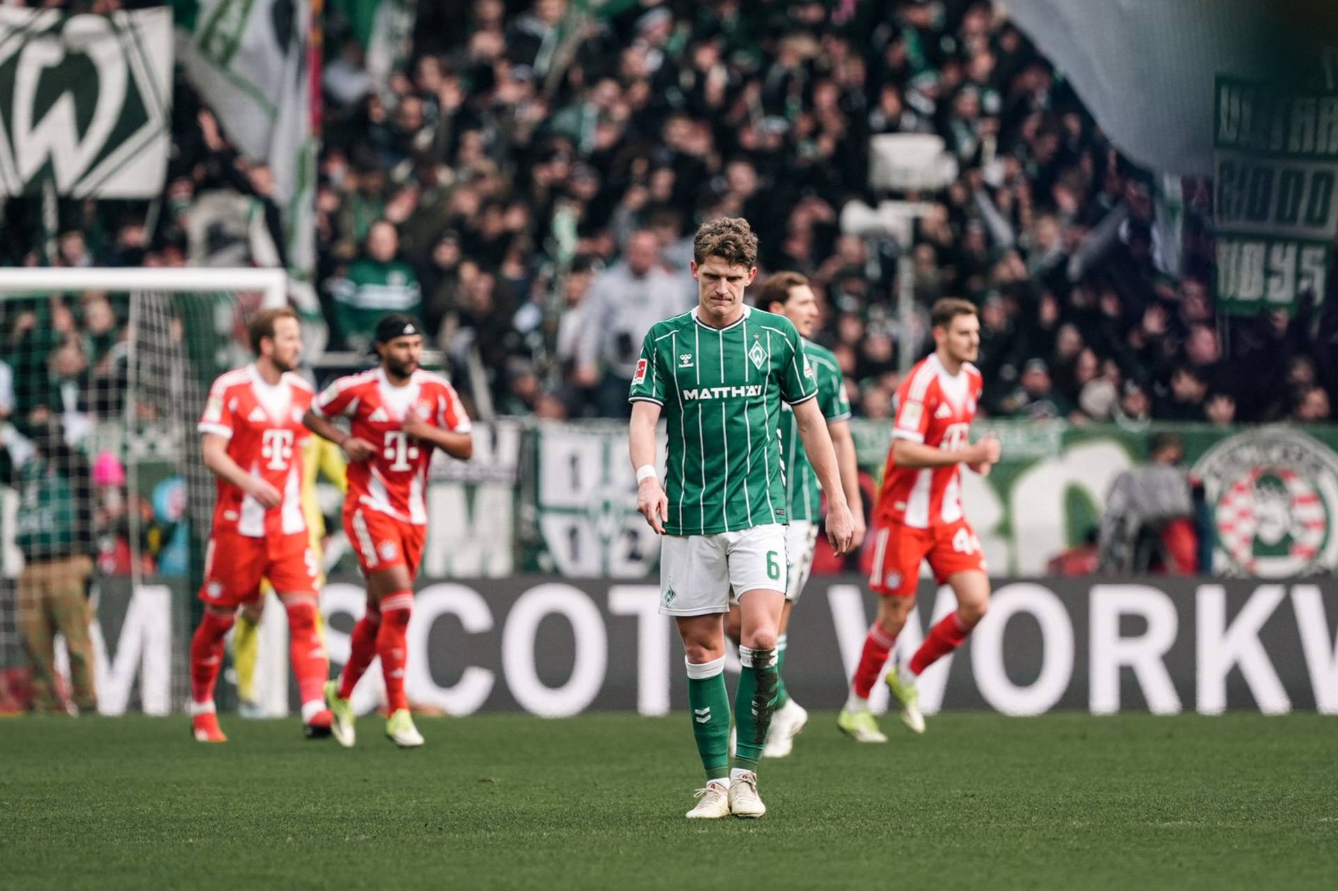 Jens Stage geht mit gesenktem Kopf in Richtung Mittelkreis, im Hintergrund die Bayern-Spieler.