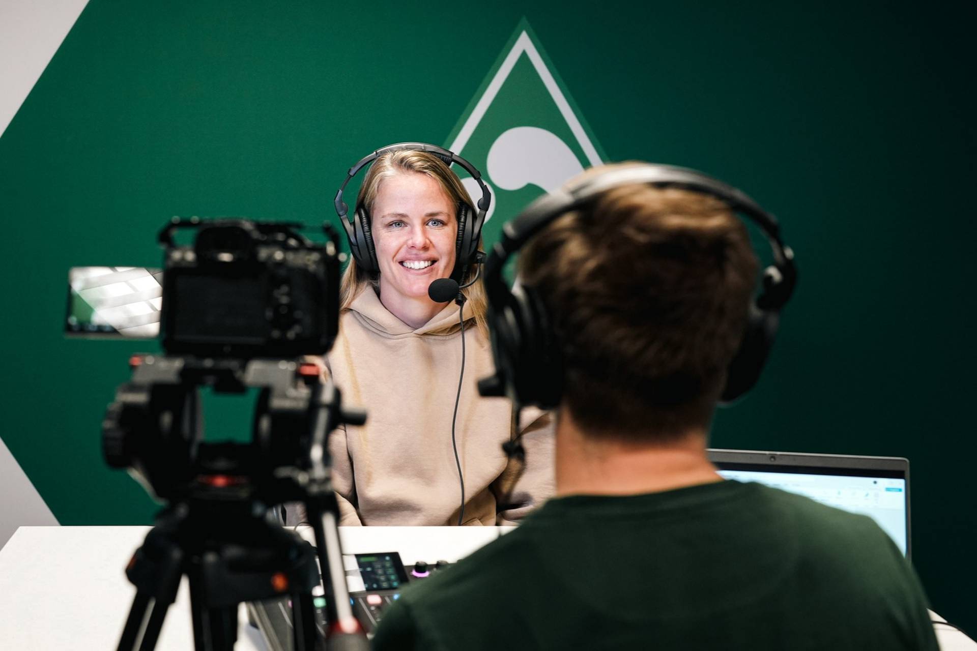 Lena Petermann mit einem Headset auf, hinter ihr ist eine Werder-Raute an der Wand.