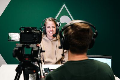 Lena Petermann mit einem Headset auf, hinter ihr ist eine Werder-Raute an der Wand.