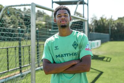 Ein Fußballspieler im grünen Trikot von Werder Bremen steht mit verschränkten Armen auf einem Fußballplatz, im Hintergrund ist ein Tor zu sehen.