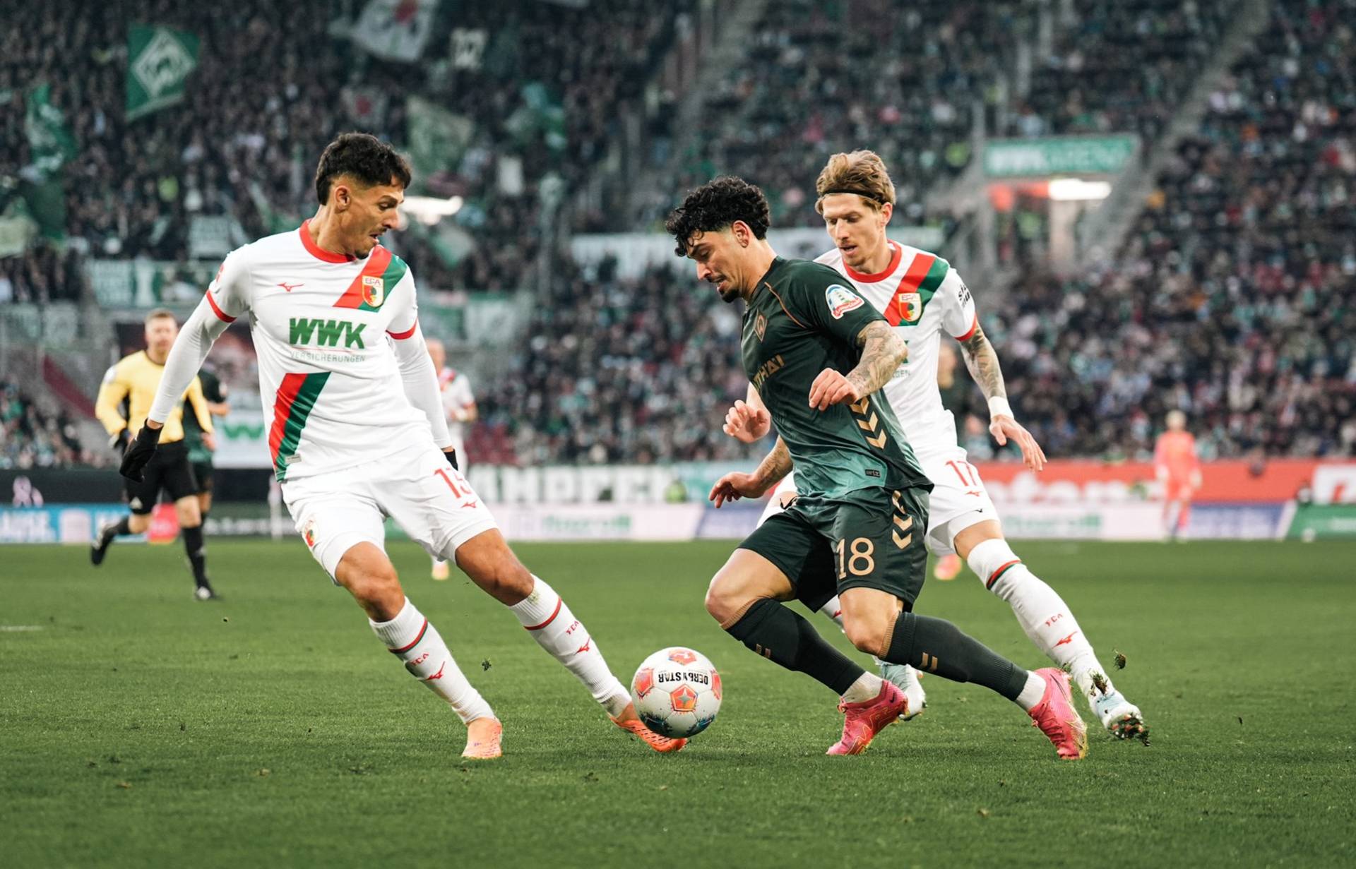 Cameron Puertas im Zweikampf mit zwei Augsburgern, er hat den Ball am Fuß.