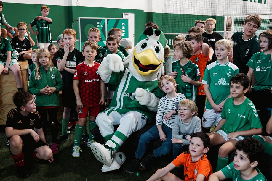 Möwe Toni sitzt umringt von Kindern, die alle Werder Trikots tragen
