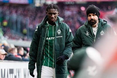 Karim Coulibaly geht mit einer Winterjacke über dem Trikot und gesenktem Kopf am Spielfeldrand. Neben ihm läuft ein Physio.