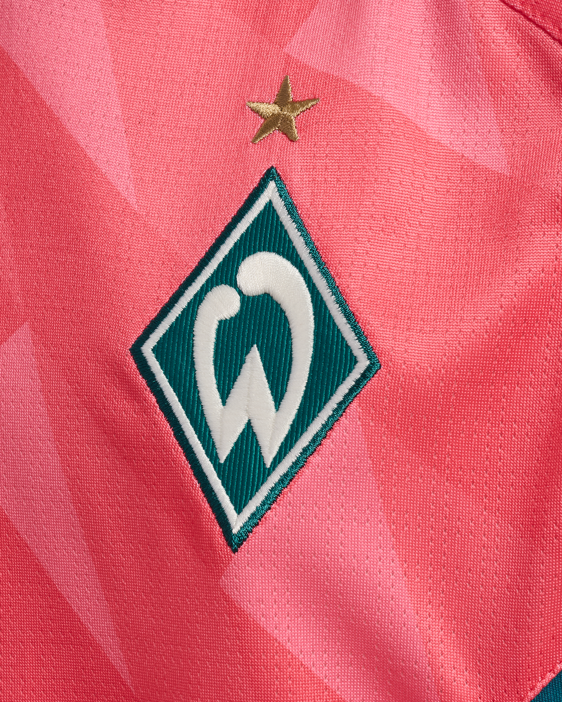 Nahaufnahme eines korallfarbenen Stoffes mit einem grün-weißen „W“-Logo und einem goldenen Stern darüber.
