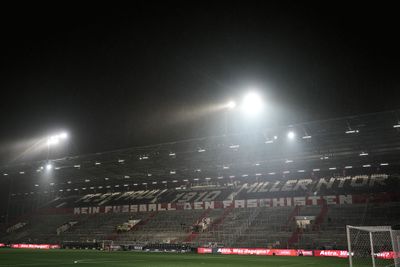 Ein leeres Stadion bei Nacht unter grellem Flutlicht, bei bewölktem Wetter und mit deutschen Aufschriften auf den Tribünen.