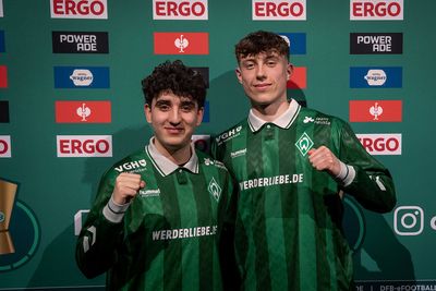Berkay und Henning stehen vor einer Sponsorenwand.
