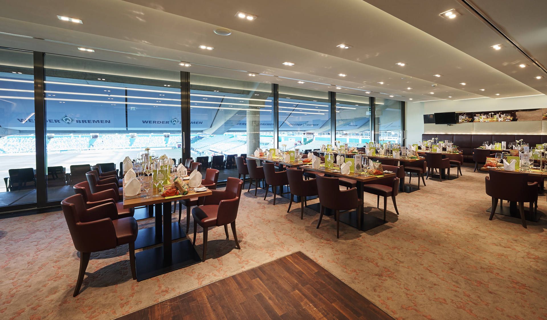 Eleganter Speisesaal mit Blick auf ein Stadion, mit Tischen, die für eine formelle Veranstaltung gedeckt sind, mit ordentlich angeordneten Stühlen und dekorativen Tischdekorationen.