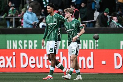 Zwei Fußballspieler in grün-weiß gestreiften Trikots laufen Seite an Seite über den Platz, umgeben von Zuschauern.