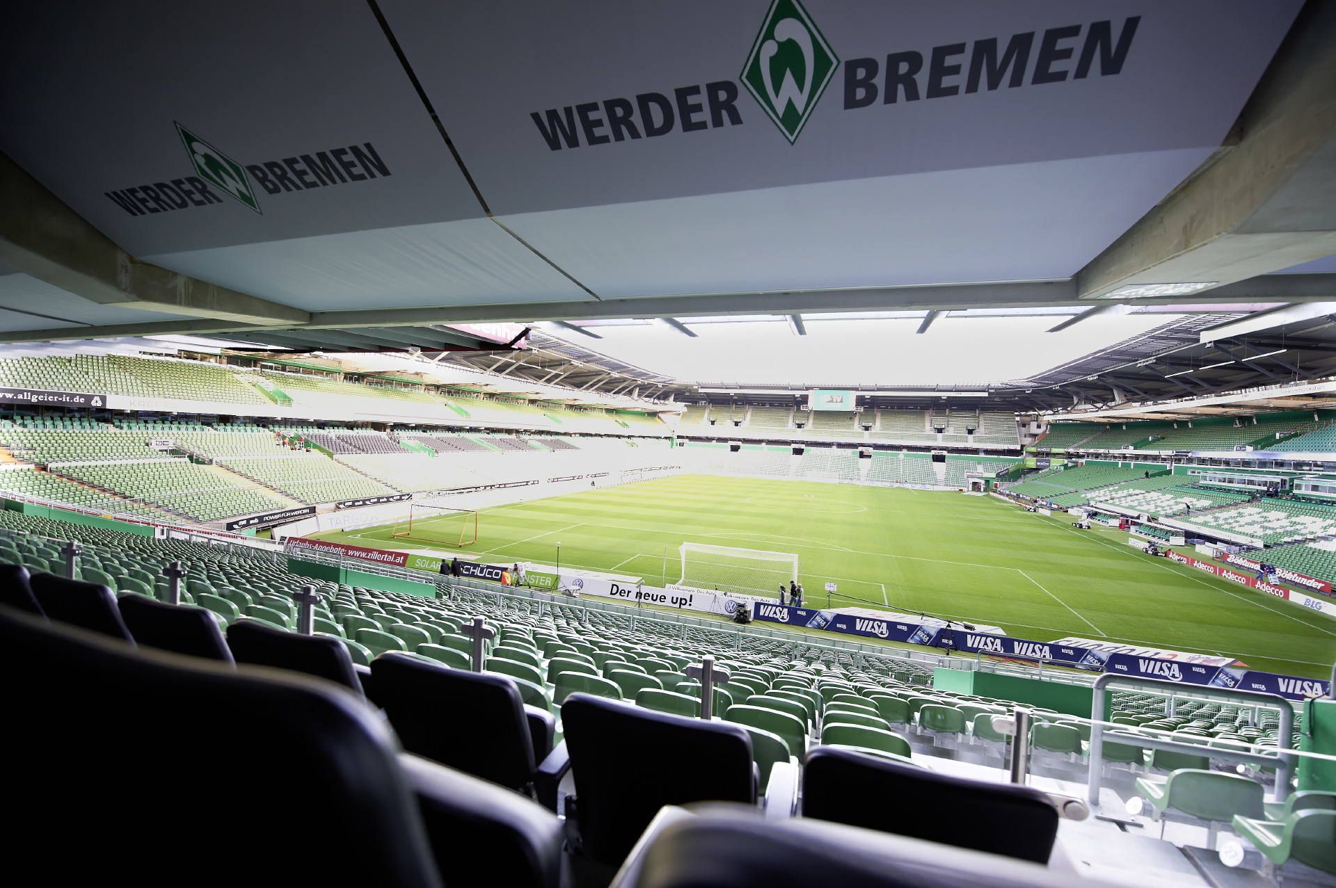 Blick auf ein leeres Fußballstadion mit grünen Sitzen und einem Werder Bremen-Logo auf dem Dach. Das Spielfeld ist gut gepflegt und bereit für ein Spiel.