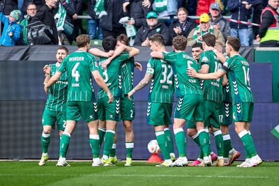 Eine Fußballmannschaft in grünen Trikots versammelt sich jubelnd auf dem Spielfeld, im Hintergrund jubeln die Fans.