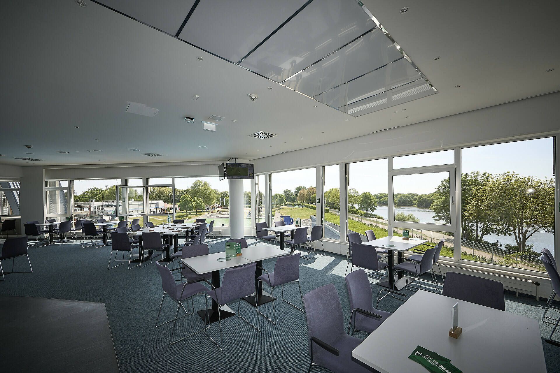 Heller Essbereich mit Tischen und Stühlen, großen Fenstern mit Blick auf Bäume und der Weser draußen.