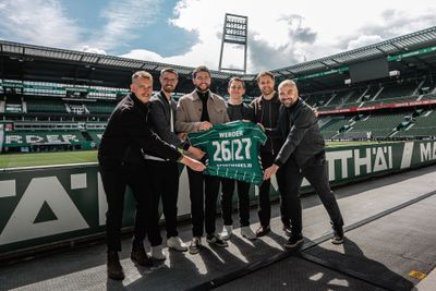 Six people inside the Weserstadion holding up a Werder shirt with 26/27 numbering and sportworks.io printing