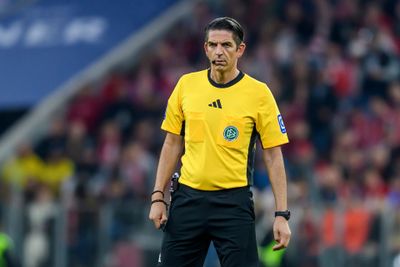 Schiedsrichter in gelbem Trikot hält auf einem Fußballfeld eine gelbe Karte hoch, im Hintergrund verschwommene Zuschauer.