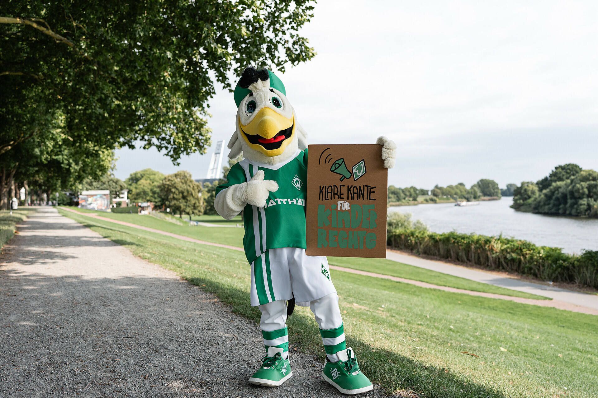 Möwe Toni hält ein Schild. Im Hintergrund ist die Weser und das Weserstadion.