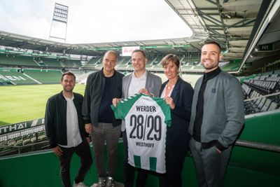 Fünf Personen stehen in einem Stadion und halten ein Trikot von Werder Bremen in den Händen, auf dem die Nummern 28/29 und der Name „Westhoff“ stehen.