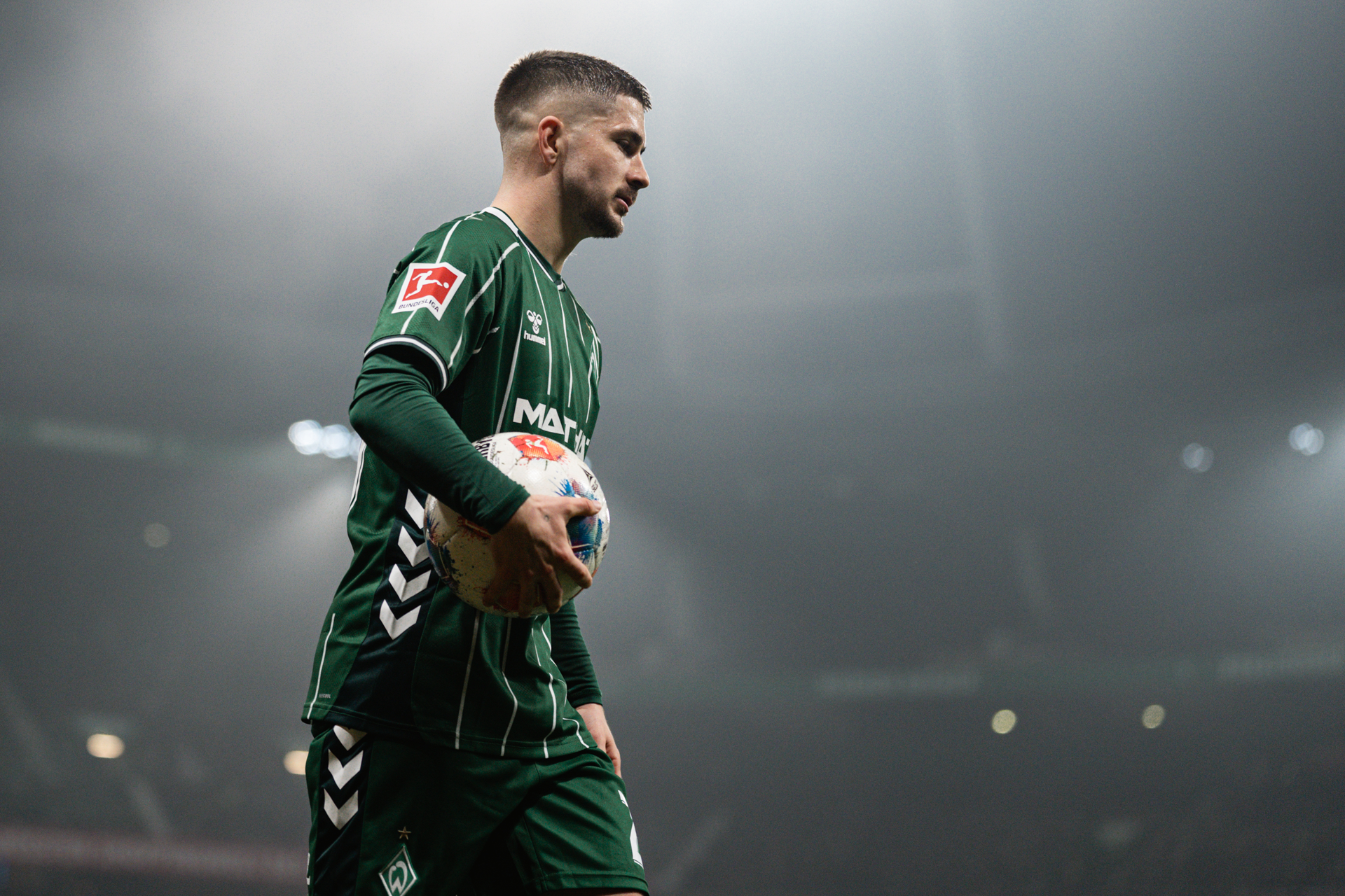 Romano Schmid hält einen Ball unterm Arm im Flutlichtschein.