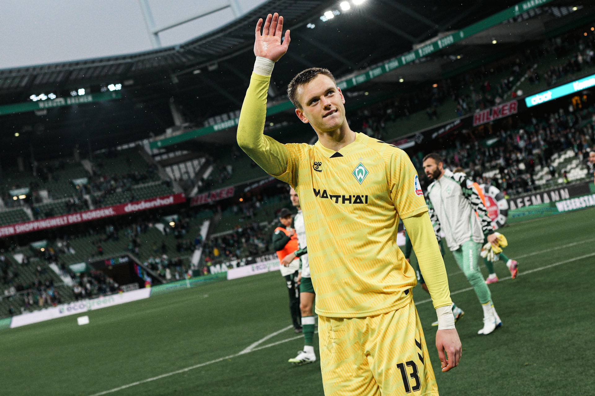 Ein Fußballspieler im gelben Trikot winkt nach einem Spiel den Zuschauern im Stadion zu.