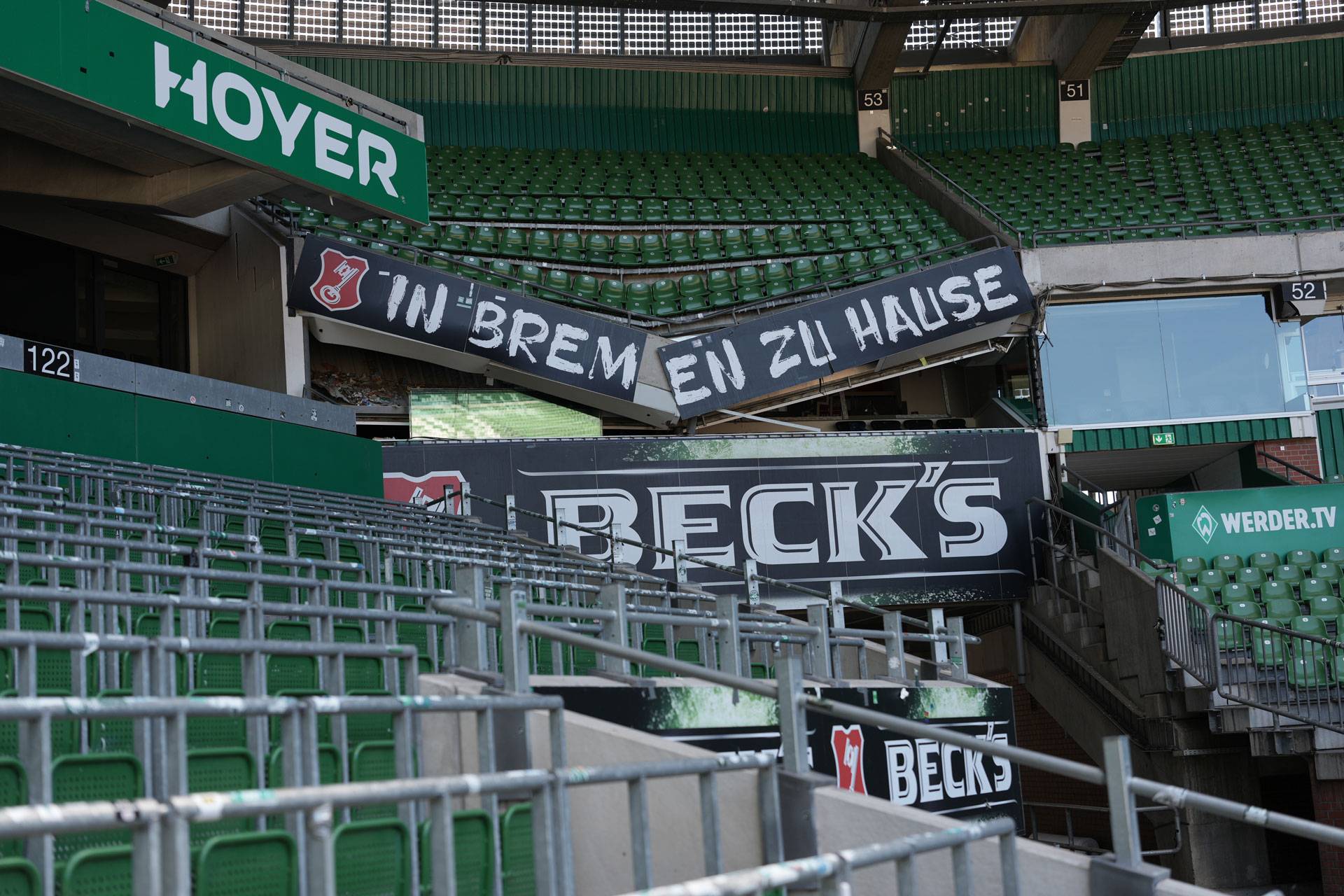 Leere Stadionplätze mit Transparenten mit der Aufschrift „IN BREMEN ZU HAUSE“ sowie Werbung für Beck’s und WERDER.TV.