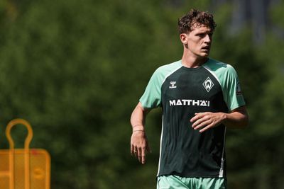 Ein Fußballspieler in einem grün-schwarzen Trikot auf einem Trainingsplatz, mit einem unscharfen grünen Hintergrund und einer orangefarbenen Trainingspuppe auf der linken Seite.