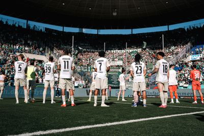 Die Fußballspieler stehen auf dem Spielfeld vor jubelnden Fans in einem großen, vollbesetzten Stadion.