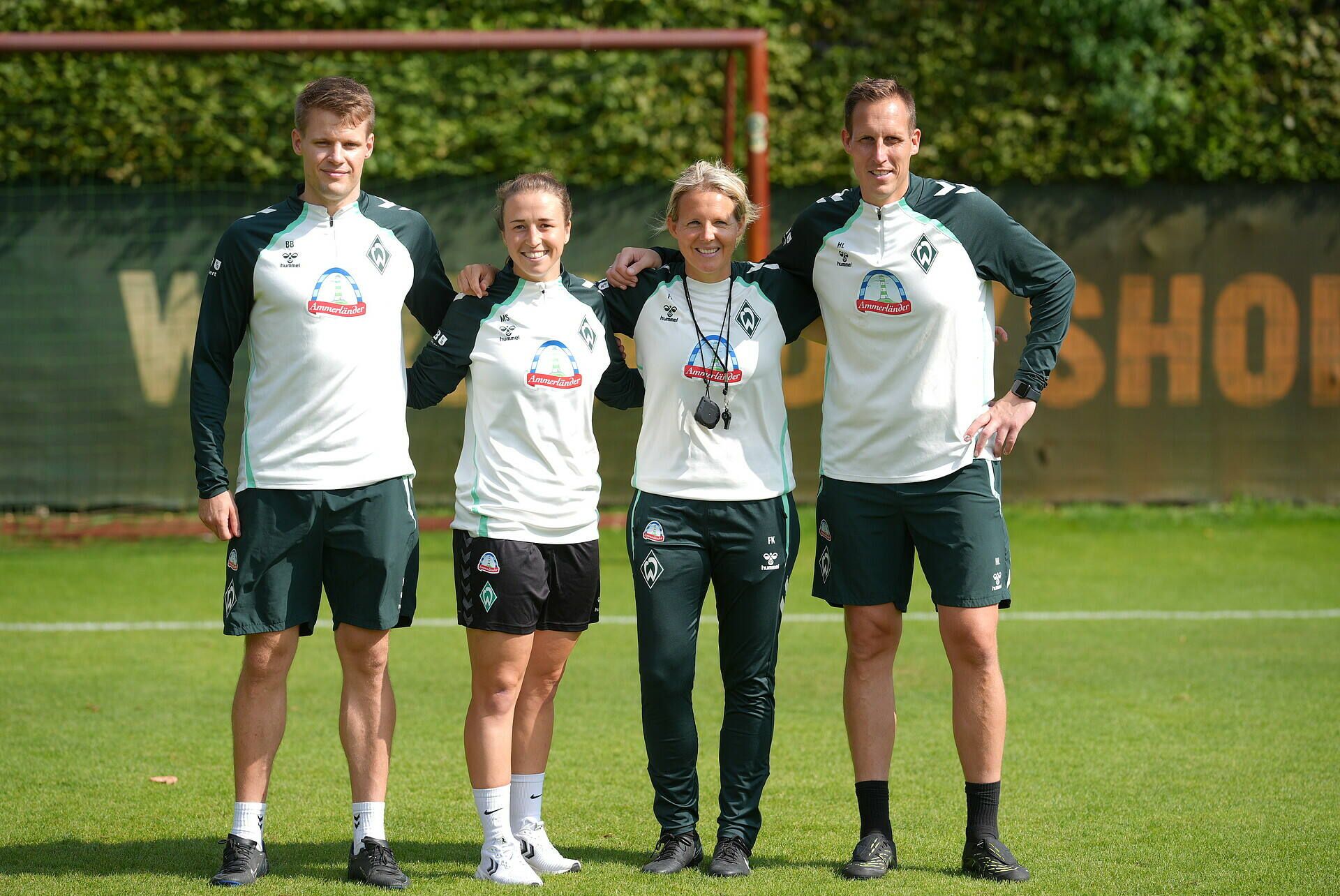 Das Trainerteam der WERDERFRAUEN steht auf Platz 11 in Trainingsklamotten. Von links nach rechts zu sehen sind: Björn Bremermann, Michaela Specht, Friederike Kromp und Hendrik Lemke. Sie stehen nebeneinander, mit den Armen über den Schultern.