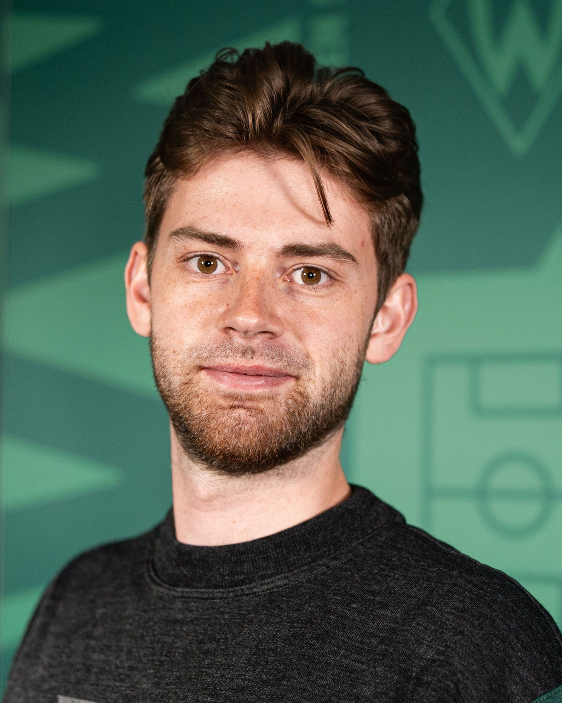 Junger Mann, der lächelt, und vor einer grünen Wand steht.