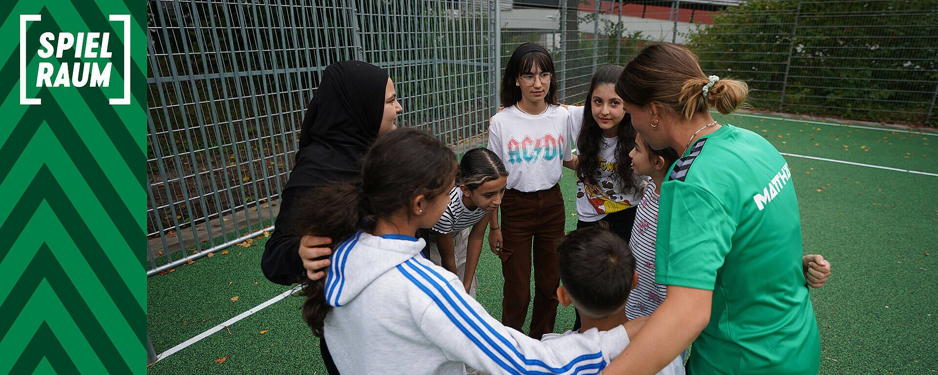Eine Gruppe von Menschen, darunter Kinder und ein Juliane Wirtz, versammeln sich auf einem Sportplatz.