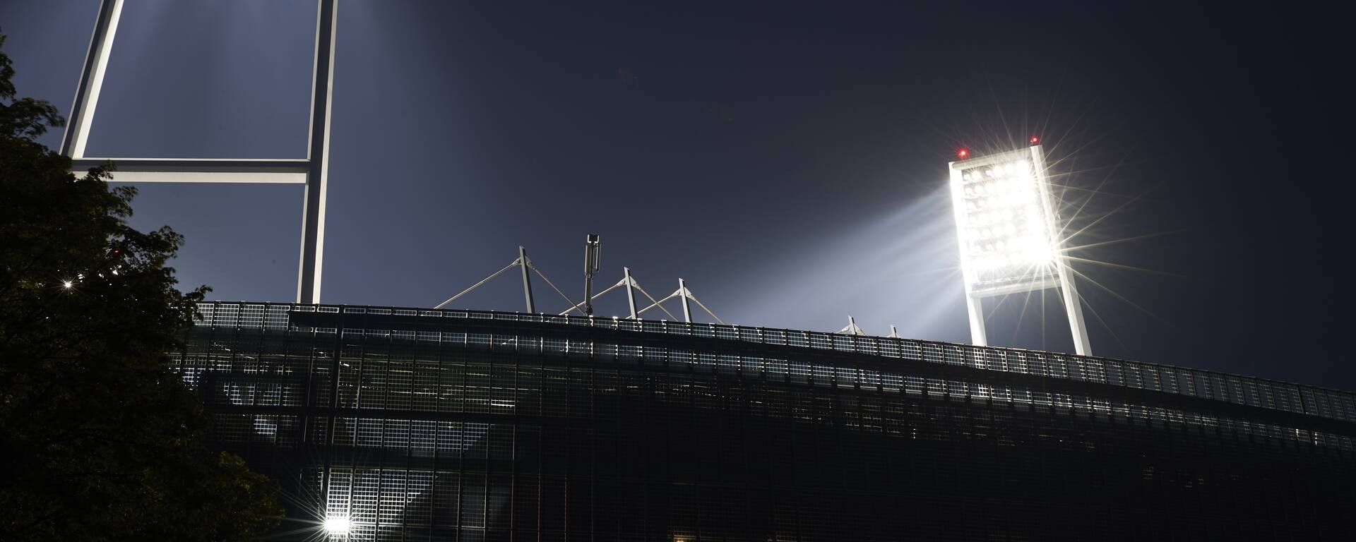 Das Stadion bei Nacht, beleuchtet von hellen Flutlichtern, die einen dramatischen Kontrast zum dunklen Himmel bilden.
