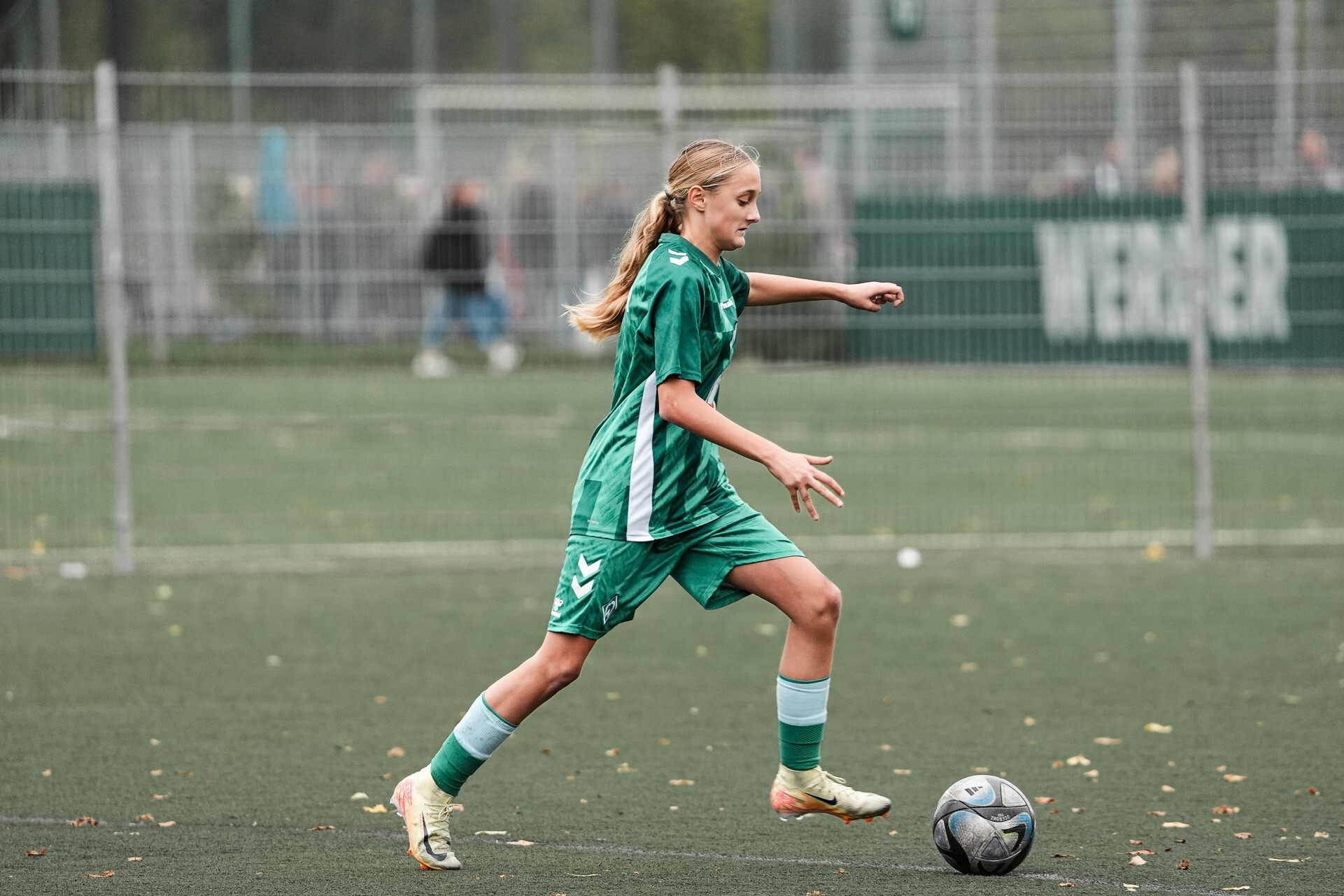 U17-Spielerin im grünen Spieldress dribbelt mit dem Ball in Richtung der rechten Bildhälfte