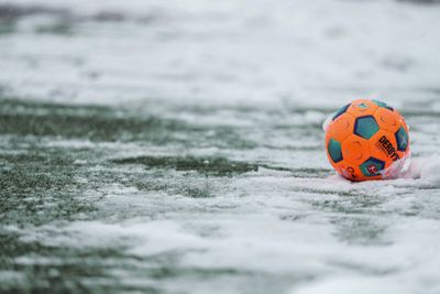 Ein orangener Fußball liegt im Schnee.