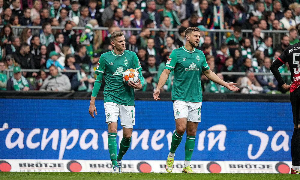 Werder-Spieler Marvin Ducksch hält den Ball in der Hand, Niclas Füllkrug hat die Arme fragend ausgebreitet.