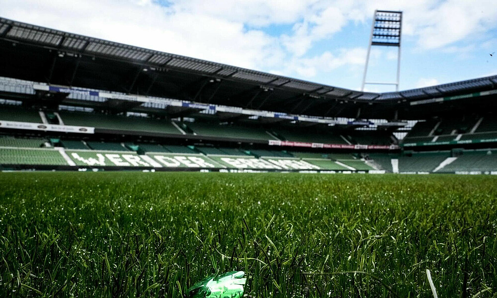 null Der Rasen im wohninvest WESERSTADION im Hintergrund ein Flutlichtmast, im Vordergrund liegt ein grünes Stück Konfetti.