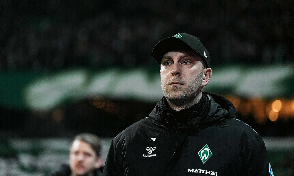 Ole Werner läuft auf das Spielfeld im Weserstadion mit Kappe vor dem Spiel gegen Augsburg, im Hintergrund die Ostkurve