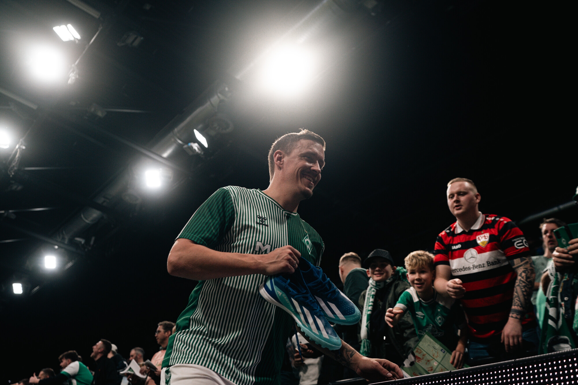 Max Kruse lächelt und hat dabei Fußballschuhe in der Hand.