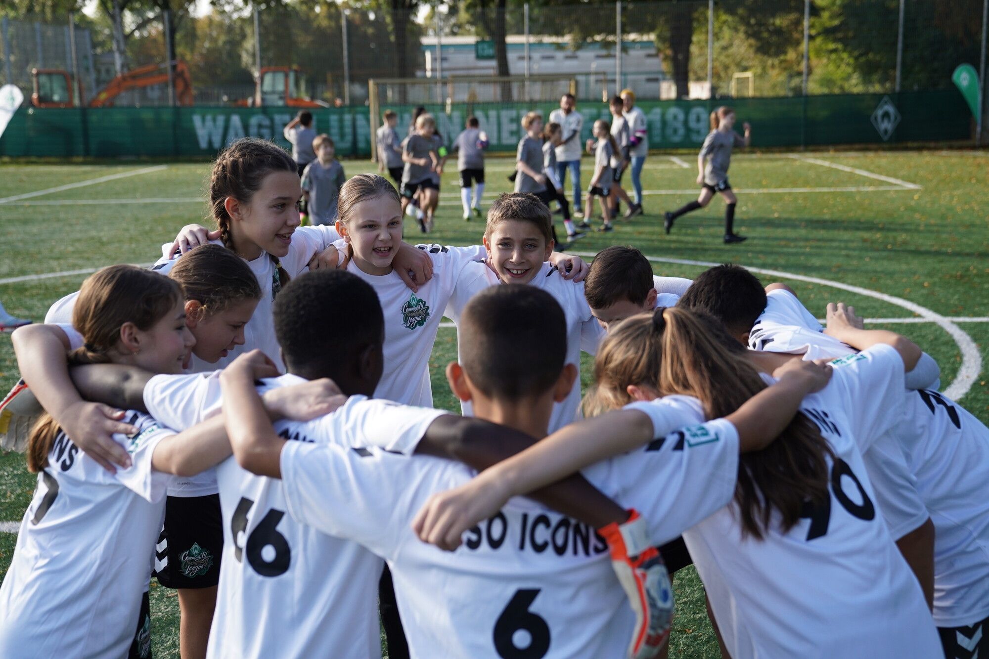 Eine Gruppe junger Fußballspieler in weißen Trikots versammelt sich auf einem Spielfeld und bereitet sich auf ein Spiel vor.