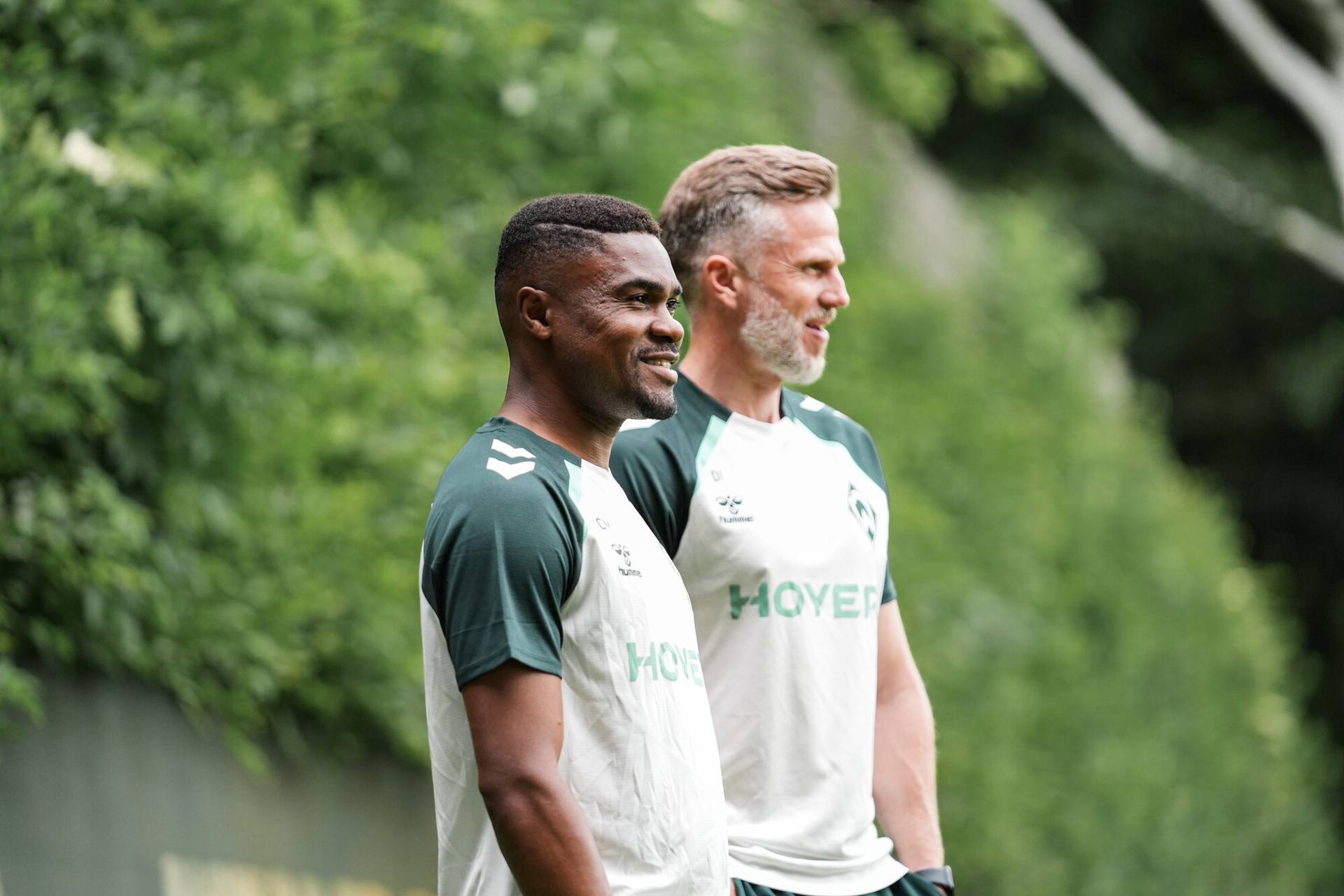 Die Werder-Trainer Cédric Makiadi und Daniel Flottmann im Seitenprofil. Beiden lächeln und gucken nach rechts.