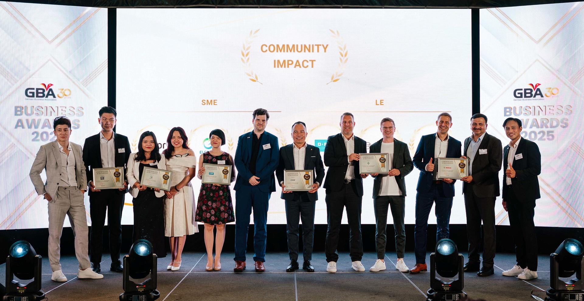 Eine Gruppe von Personen steht auf einer Bühne und hält Zertifikate bei den GBA Business Awards 2025 in der Kategorie „Community Impact“ in den Händen.