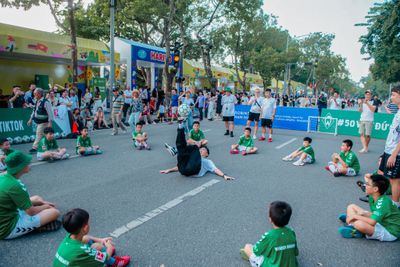 Eine Gruppe Kinder in grünen Trikots sitzt im Kreis um einen Jungen herum, der mit einem Ball jongliert