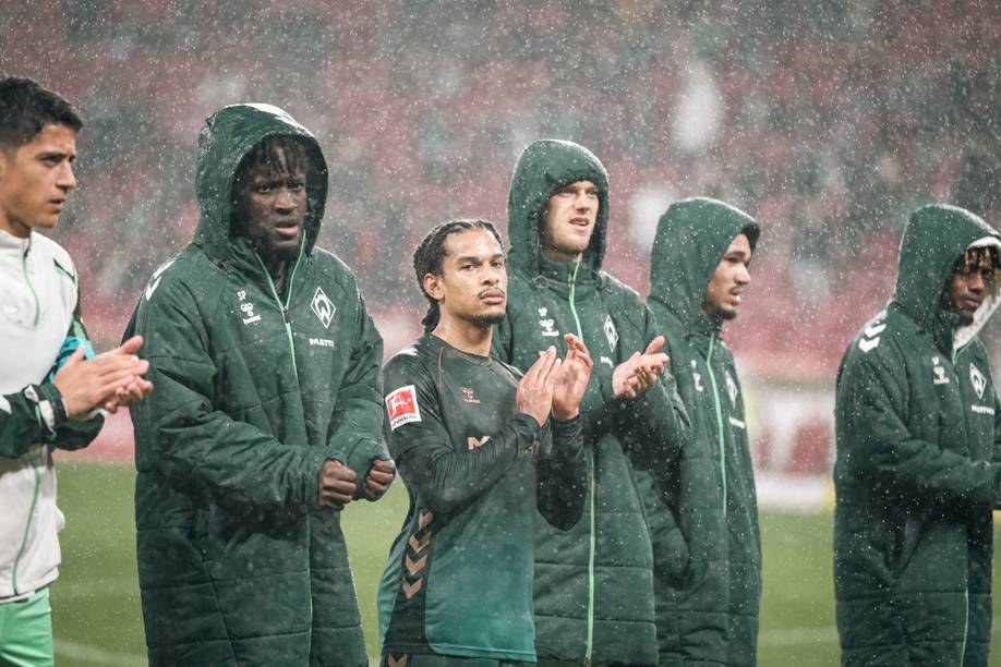 Die Werder-Profis stehen vor der Gästekurve im Regen.