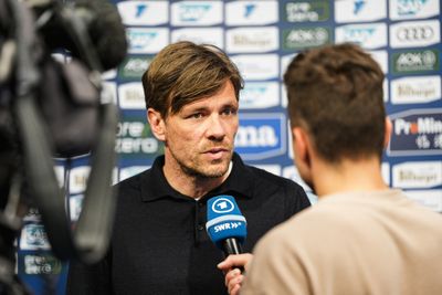 Ein Mann in einem schwarzen Hemd wird von einem Journalisten interviewt, der ein blaues SWR-Mikrofon in der Hand hält; hinter ihm ist ein Hintergrund mit einem Logo zu sehen.