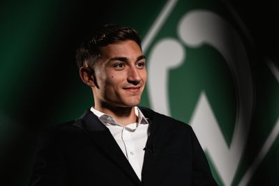 Ein lächelnder Mann im Anzug vor einem grün-weißen abstrakten Hintergrund.