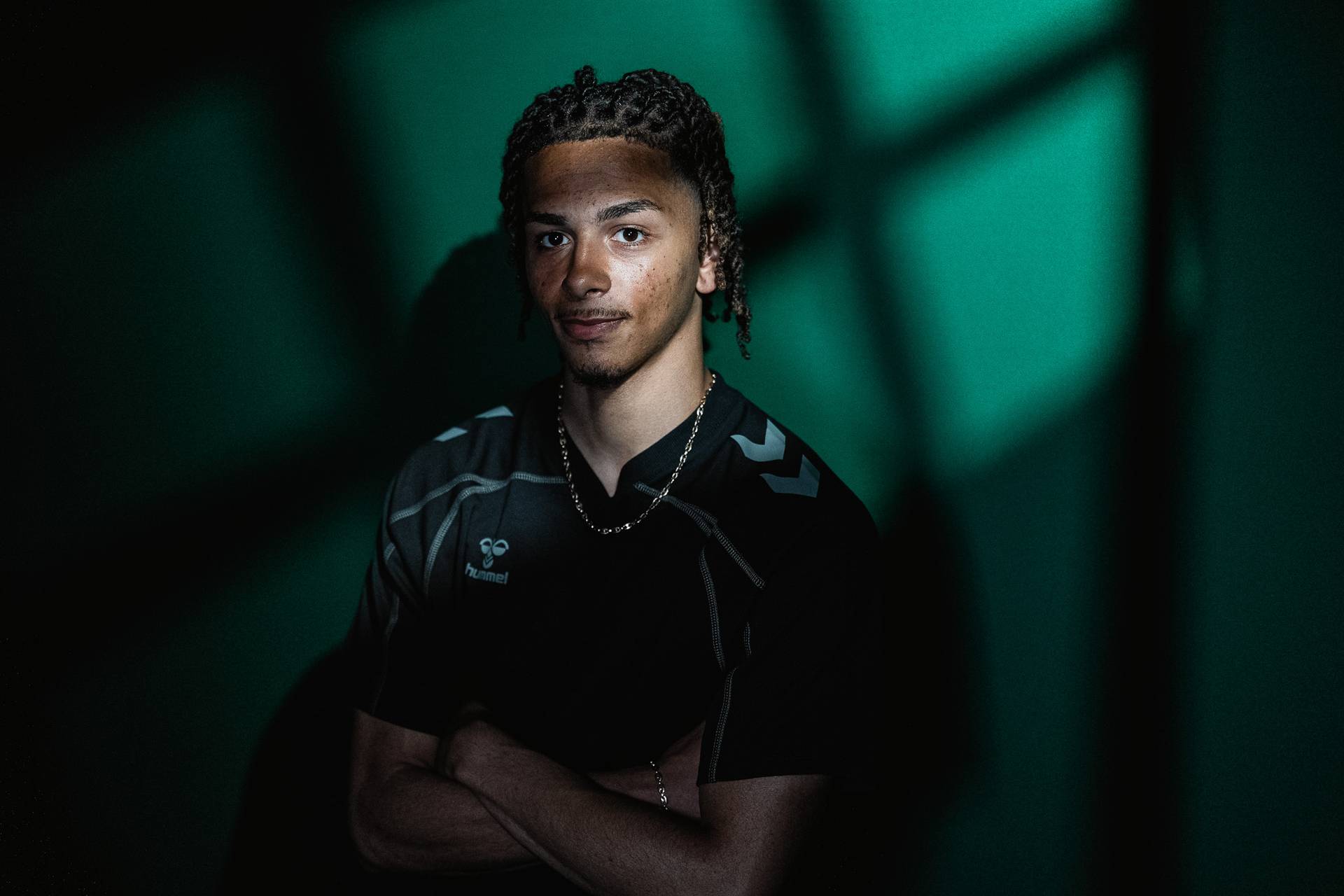 Kenny Quetant stands in front of a green wall with his arms crossed.